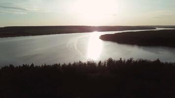 Wide and quiet river is located between the fields and forests at sunrise. A small house stands on the bank of the river with a beautiful view of the countryside. Aerial view. video