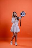 full body beautiful ladies white top standing full shout holding megaphone loudspeaker forward and mic audio isolation orange background. for technology concept, advertising, broadcast, promotion photo