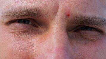 Close up to upset male face looking into camera with a disappointing sight. Upset facial expression of man with blue eyes. Unhappy gaze of despairing young guy. Slow motion photo
