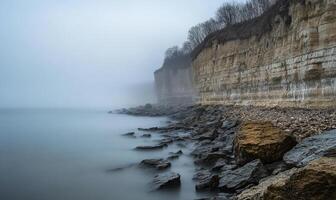 A foggy shoreline with a rocky beach and a cliff photo