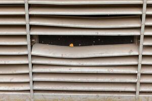 A close-up of a metal vent with a small piece of orange debris visible through the mesh screen photo