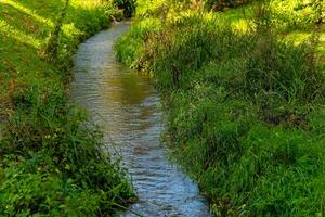 A small stream winds through a grassy field, creating a tranquil scene photo