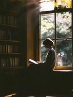 A woman sitting in front of a window reading a book photo
