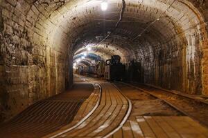 An old abandoned mine tunnel features rusty metal rails and rough stone walls, creating a dark and spooky atmosphere that evokes a sense of history and mystery. photo