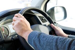 A person is driving a vehicle. The image focuses on the steering wheel and the persons hands, highlighting the act of driving and the details of the vehicles interior. photo