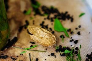 A closeup of a dried butterfly pupa on a wooden table. The pupa is brown and has a wrinkled texture. There are scattered tea leaves and a green leaf on the table. photo