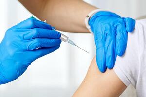 A healthcare professional in blue gloves administers a vaccine to a patient wearing a white T-shirt. The scene emphasizes the importance of vaccinations in promoting public health and wellness. photo