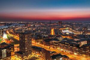 A stunning cityscape showcases modern skyscrapers along a river, illuminated by the warm glow of the setting sun, creating a vibrant and energetic atmosphere in the heart of the city. photo