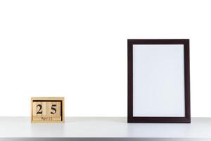 Wooden calendar 25 april with frame for photo on white table and background