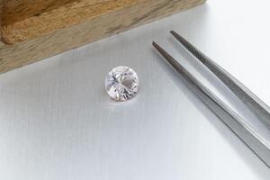 macro mineral faceted stone Morganite with tweezers on a gray background photo