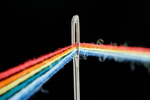 multi-colored threads for sewing in the form of a rainbow pass through an antique needle on a black background photo