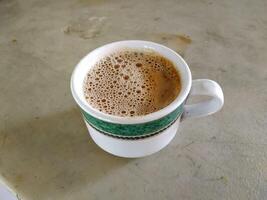 A cup of frothy coffee in a white mug with a green decorative band, placed on a textured surface. photo