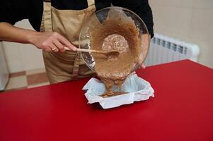 Person pouring cake batter into a baking tray on red surface photo