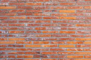 Brick wall made of red and orange bricks arranged horizontally with gray mortar in between. The bricks are slightly weathered, showing signs of wear and discoloration. photo