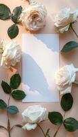 White Roses and a Blank Card Surrounded by Green Leaves on a Pale Peach Background photo