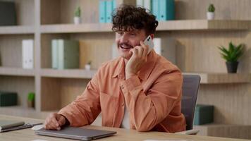 Smiling Caucasian man business worker employer guy male entrepreneur consult client cellphone conversation talk mobile phone in office happy cheerful businessman smartphone call chatting speak laugh video