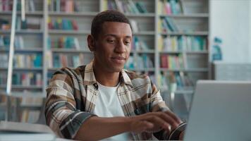 contento africano americano hombre chico estudiante biblioteca alto colegio Universidad estudiando aprendizaje sonrisa mecanografía cerca ordenador portátil terminar trabajo diploma hecho lograr aprendiz computadora e-learning en línea proyecto masculino alumno video