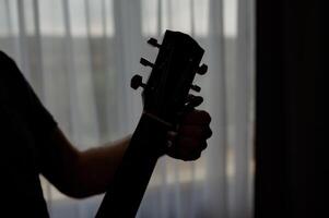 Silhouette of guitarist paying a acoustic guitar against window. Man musician in studio on music instrument photo