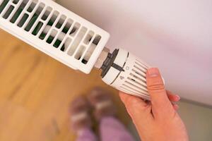 A hand adjusts the temperature on a radiator thermostat, marking the start of the heating season. photo