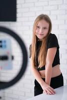 Beautiful teenage girl posing in front of a phone on a tripod. Child blogger shoots in front of camera and ring lamp photo