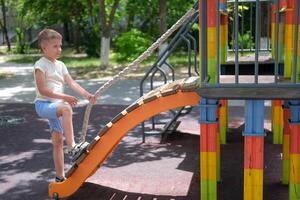 A child plays on the playground. A little boy climbs a children's slide on a rope. photo