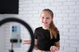 Beautiful teenage girl posing in front of a phone on a tripod. Child blogger shoots in front of camera and ring lamp photo