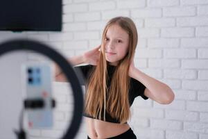 Beautiful teenage girl posing in front of a phone on a tripod. Child blogger shoots in front of camera and ring lamp photo