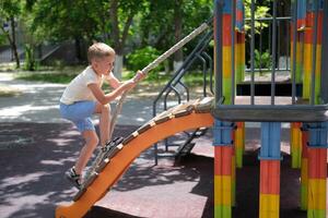 A child plays on the playground. A little boy climbs a children's slide on a rope. photo