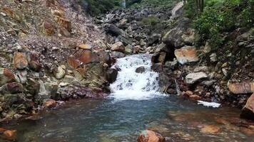 The low-flying drone moves forward above a small river with clear, fresh water and many scattered mountain rocks and surrounded by green forest. video