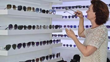 Eyewear browsing, woman trying on sunglasses, surrounded by a wide variety of styles, modern store setting, evaluating personal appearance, enjoying retail experience, fashion-forward choice video
