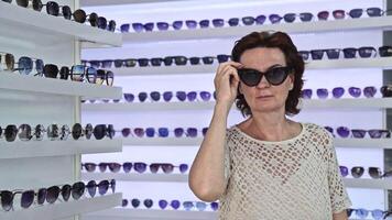 Woman testing sunglasses in store, surrounded by multiple styles, modern layout, personal fashion choice, browsing eyewear collection, enjoying retail atmosphere, checking appearance video