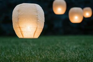 Glowing lanterns floating in the night sky over a grassy field photo