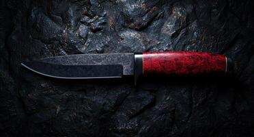 Closeup of a sharp knife with a red wooden handle on a dark background photo