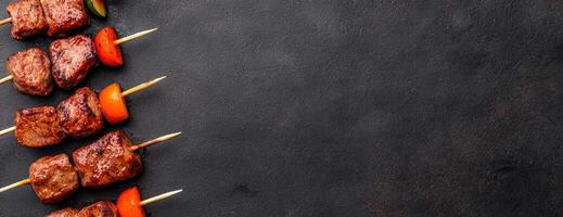 Grilled meat skewers with vegetables on dark background photo