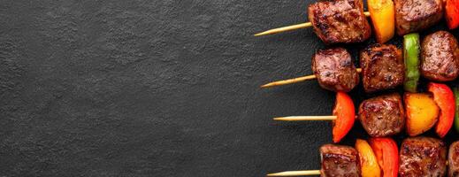 Grilled meat and vegetable skewers on black background photo