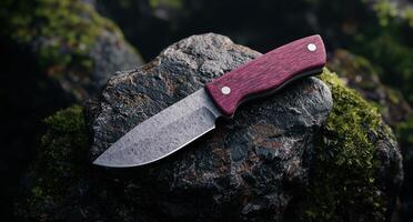 Closeup of a sharp survival knife with a red wooden handle on a mossy rock photo