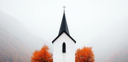 white church with black spire surrounded by autumn trees photo