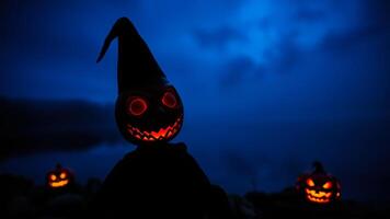 glowing jack-o-lantern with a pointed hat stands against a dark blue sky photo