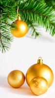 three gold ornaments resting on a white surface with a pine branch photo