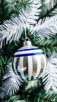 shiny striped christmas ornament hanging on a festive pine tree branch photo