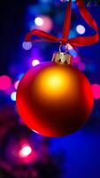 red ornament with a golden top hangs from a red ribbon against a blurry background lights photo