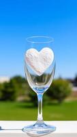 clear wine glass holds a white heart against a blue sky photo