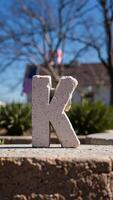 large concrete letter 'k' stands on a stone wall photo