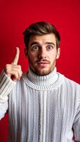 man a white sweater points upward with a surprised expression photo
