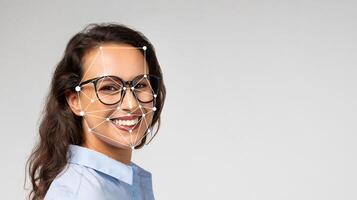 A woman with glasses is smiling while technology captures her facial features. She is in a well-lit studio, showcasing the advancement in facial recognition capabilities. photo