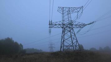 A quiet rural area features towering transmission lines looming over a foggy landscape, creating an atmospheric and serene early morning setting. video