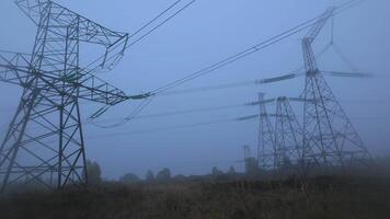 Early morning in a rural area reveals towering power lines partially obscured by thick fog, creating an atmospheric and serene landscape. The scene captures the stillness of nature. video
