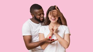 Surprise Proposal. Romantic Black Guy Covering Eyes And Giving Engagement Ring To His Excited Girlfriend, Yellow Background With Copy Space photo