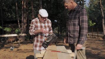 Two men engage in a woodworking project outdoors, surrounded by trees. The older man shares his expertise as they work together on a wooden piece, fostering a connection through craftsmanship. video