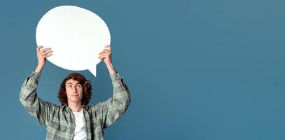 Attractive teenage guy holding speech bubble with empty space for your design, turquoise background photo